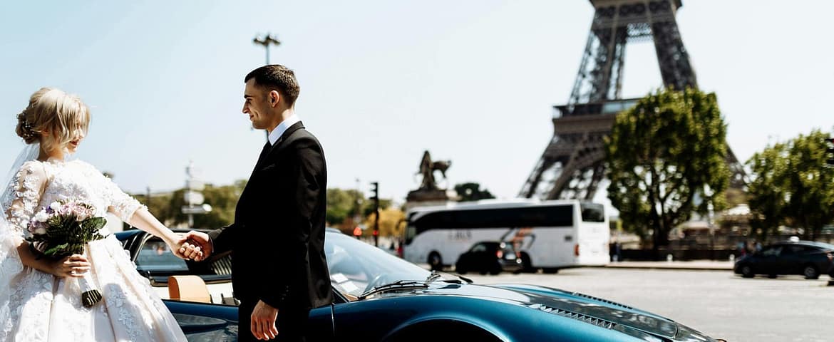 A romantic couple's wedding day captured near the Eiffel Tower in Paris with a luxury car in the foreground.