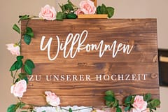 pexels-photo-14365407-14365407 Wooden welcome sign adorned with pink roses for a wedding celebration.